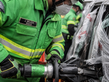 Load image into Gallery viewer, Person in green rescue uniform using a tool on a vehicle