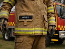 Load image into Gallery viewer, Firefighter in brown uniform with 'Arnold' name tag, standing in front of a fire truck.
