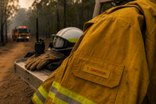 Load image into Gallery viewer, Firefighter in yellow jacket with helmet and radio on a truck during a fire incident.
