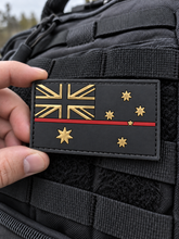 Load image into Gallery viewer, Hand holding a thin red line Australian flag PVC patch against a tactical backpack
