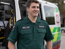 Load image into Gallery viewer, Man in a green uniform standing in front of an ambulance
